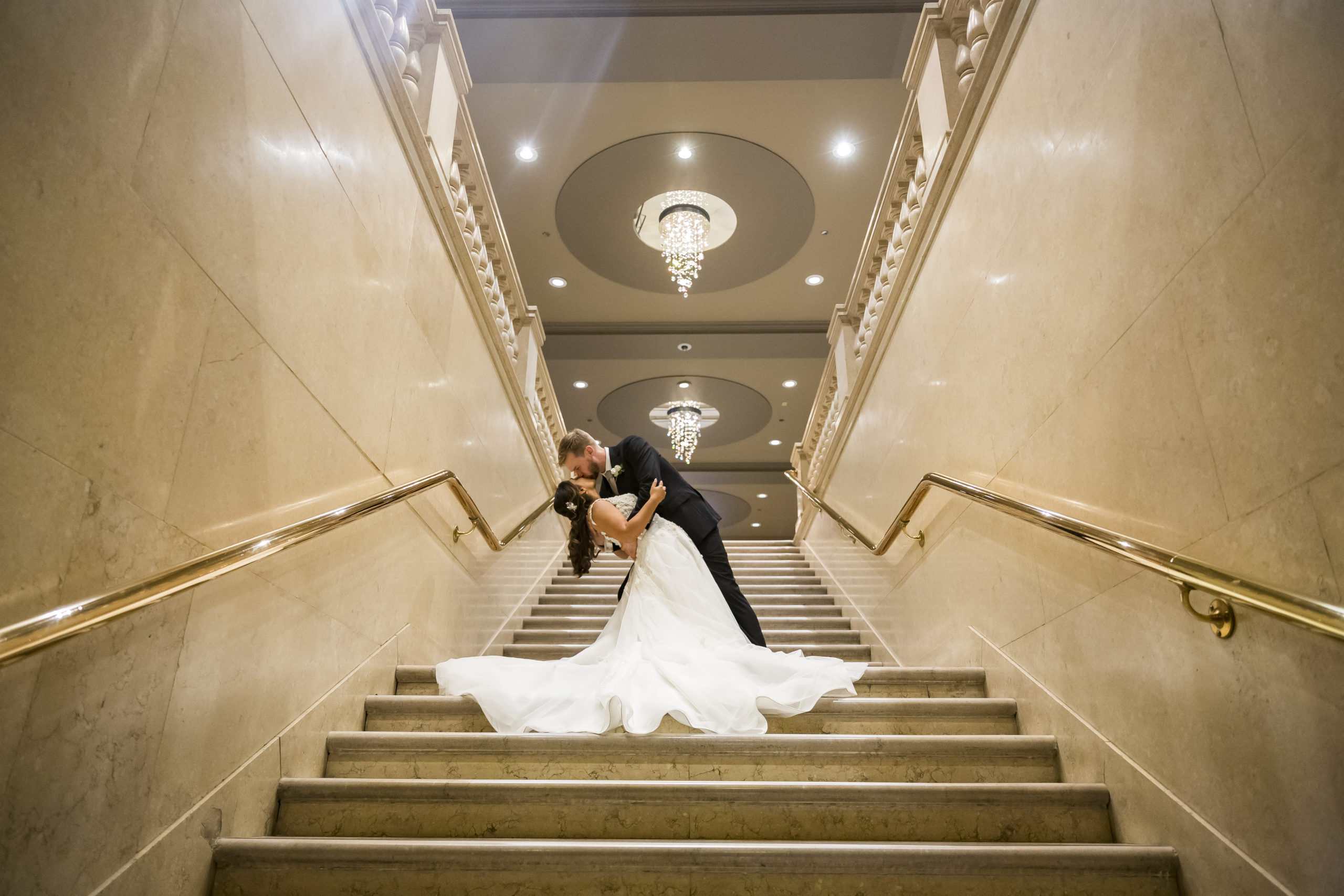 A bride and groom kiss on the grand staircase during their One King West wedding